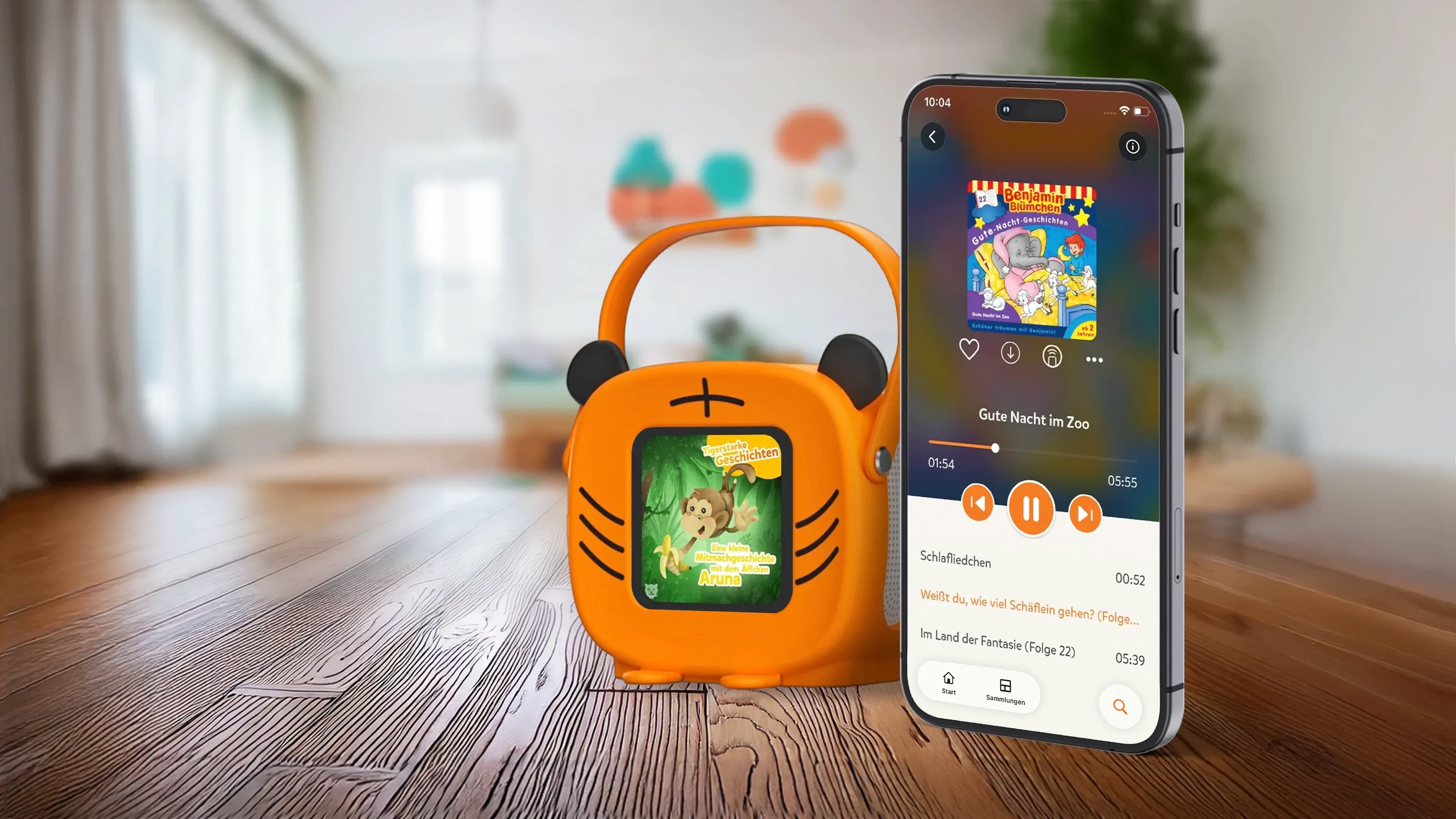 tigerbox MINI mit Tiger-Hülle auf Holzboden, daneben ein Smartphone, das die Hörbuch-Einstellungen anzeigt. 