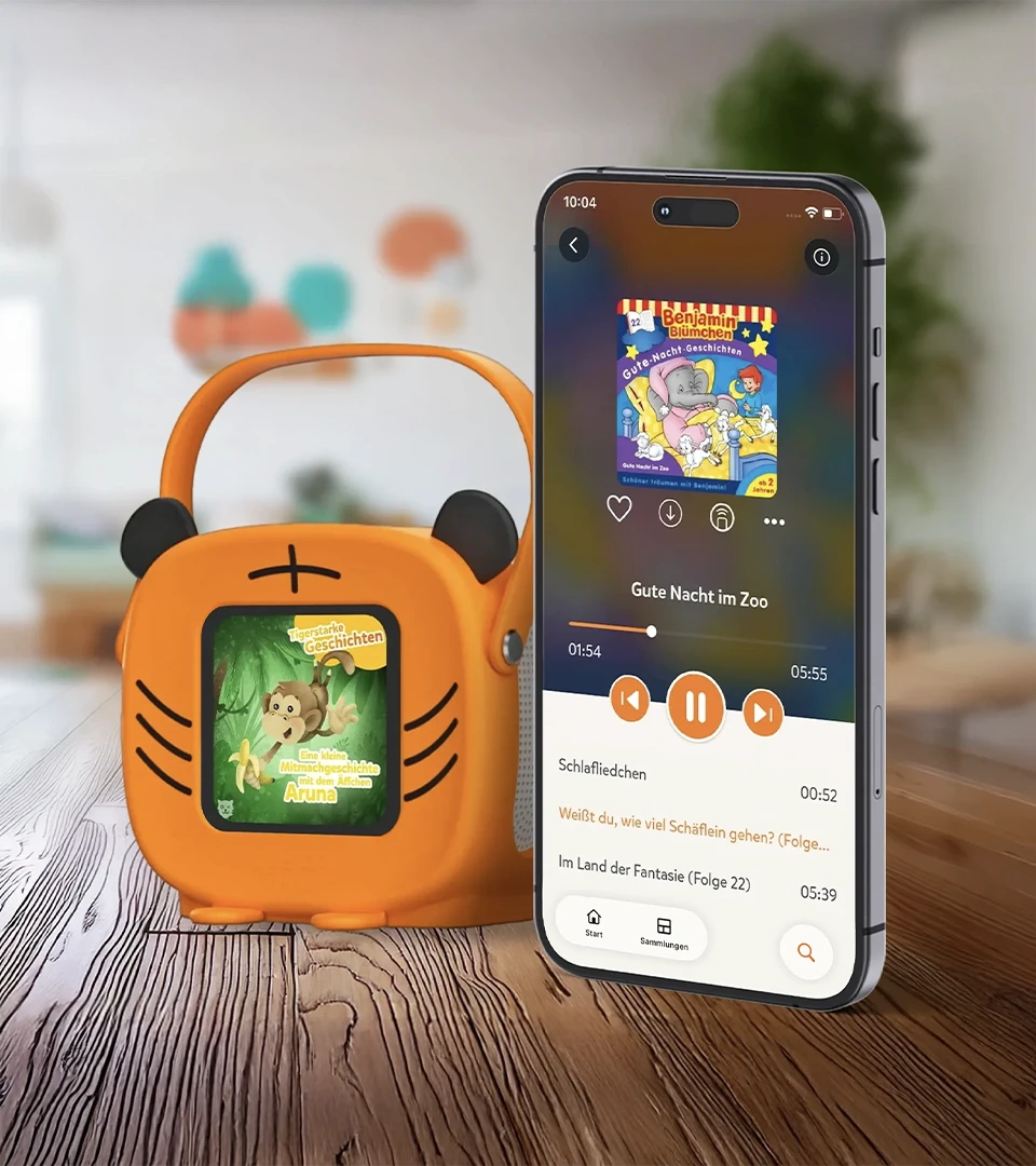 tigerbox MINI mit Tiger-Hülle auf Holzboden, daneben ein Smartphone, das die Hörbuch-Einstellungen anzeigt. 